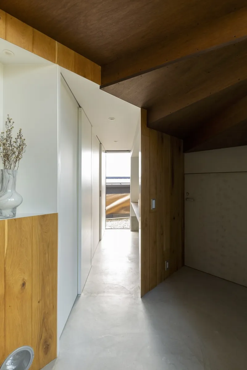 Ground-floor corridor: white sliding door, timber-lined alcove with dried flowers in a ceramic vase, concrete floor, exposed timber structure above