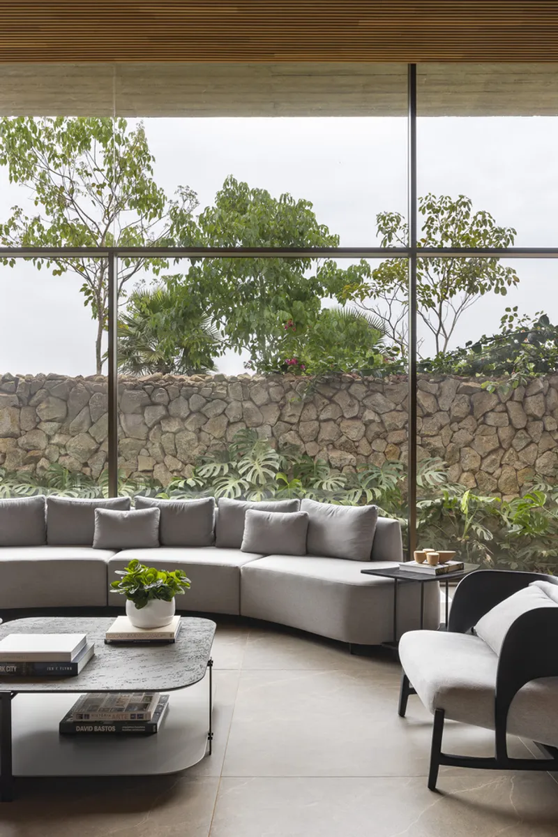 Living area seating facing gabion stone wall and tree canopy through frameless glass wall