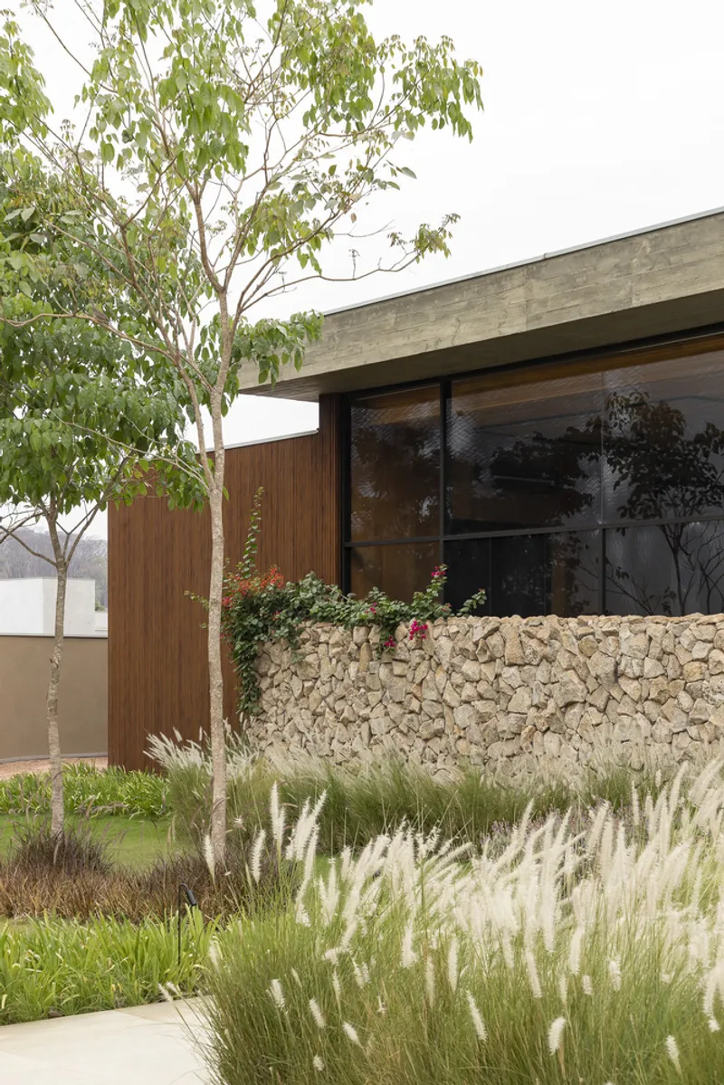 Exterior corner showing concrete overhang above timber-clad wall and gabion base with planted grasses