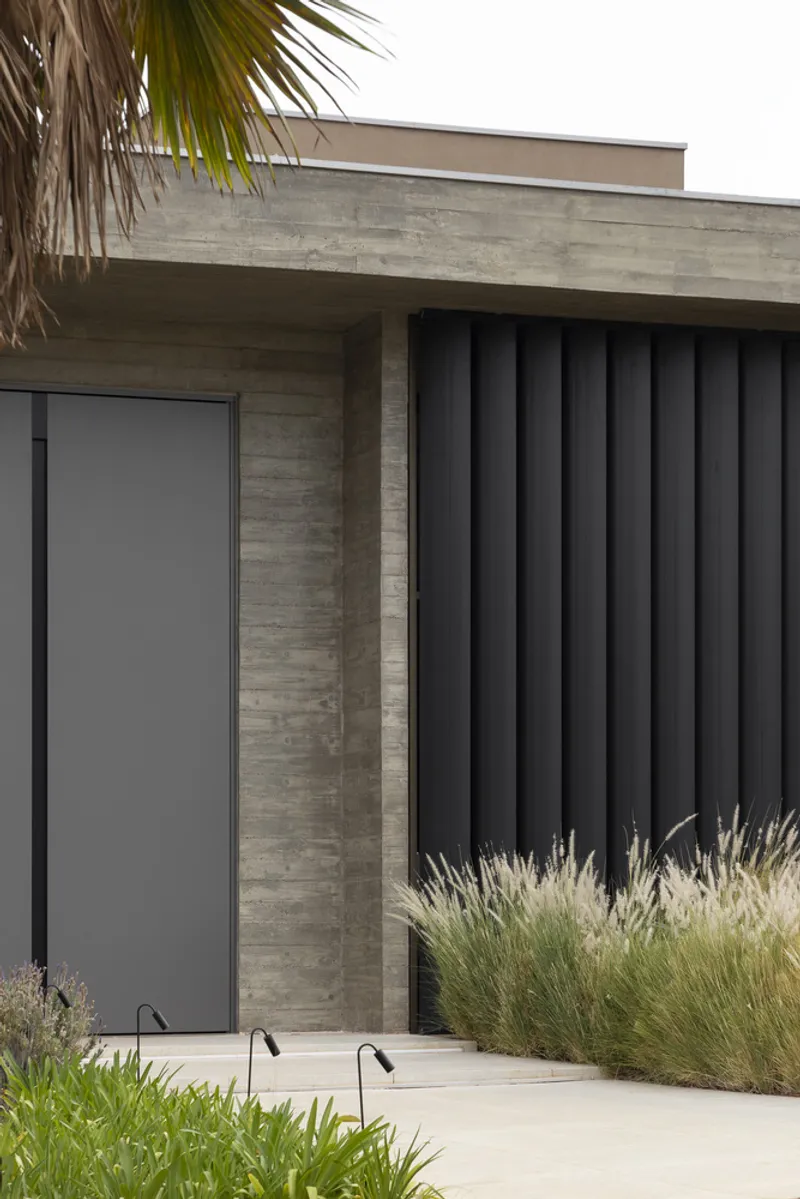 Front elevation showing board-formed concrete entrance and vertical charcoal cladding beside native grasses