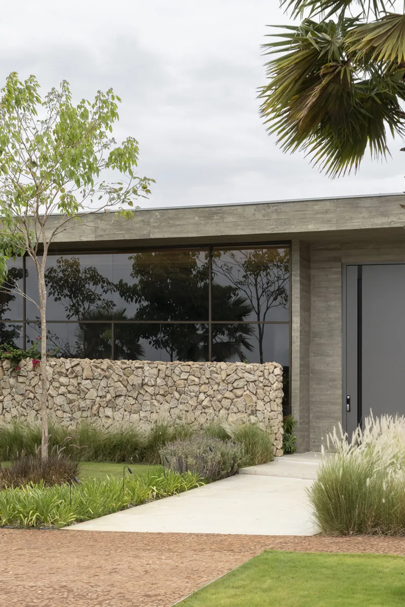 Street view of the board-formed concrete facade with stone gabion wall and plantings framing the entrance path