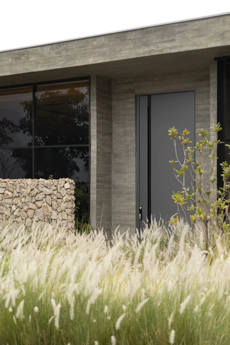 Entry door set in board-formed concrete pillar with ornamental grasses in the foreground