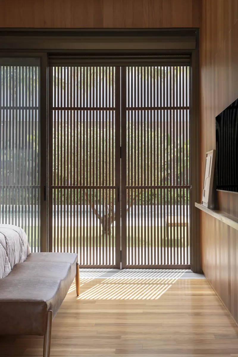 Bedroom interior showing vertical slatted screen doors filtering afternoon sunlight across timber floor