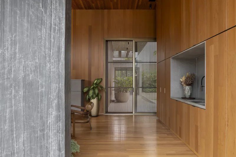 Timber-lined corridor with vertical slatted doors filtering daylight from the courtyard beyond
