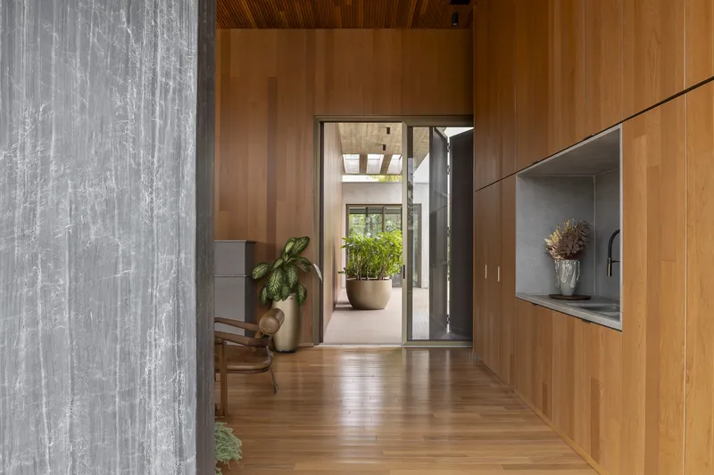 View through open timber-framed doorway revealing a concrete passage and planted entry courtyard