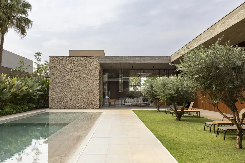 Rear facade with gabion stone wall and concrete roof overhang beside the lawn and pool