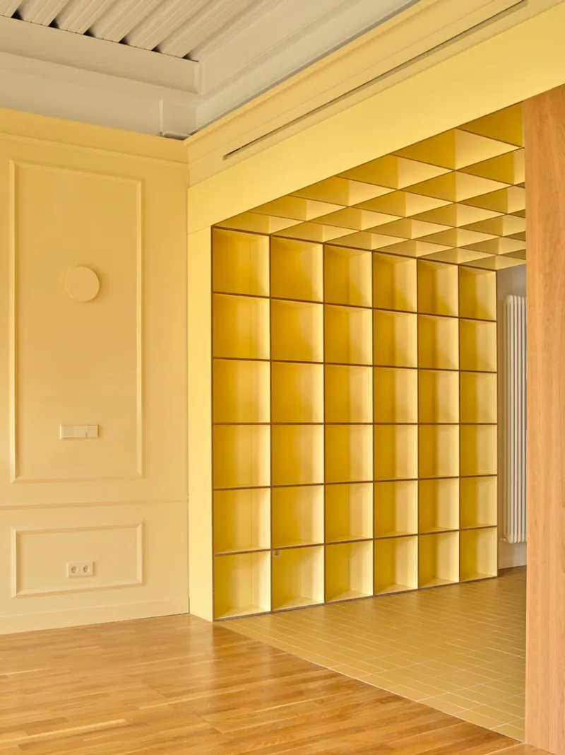 Yellow gridded shelving unit recessed in wall opening with timber frame and slatted ceiling above