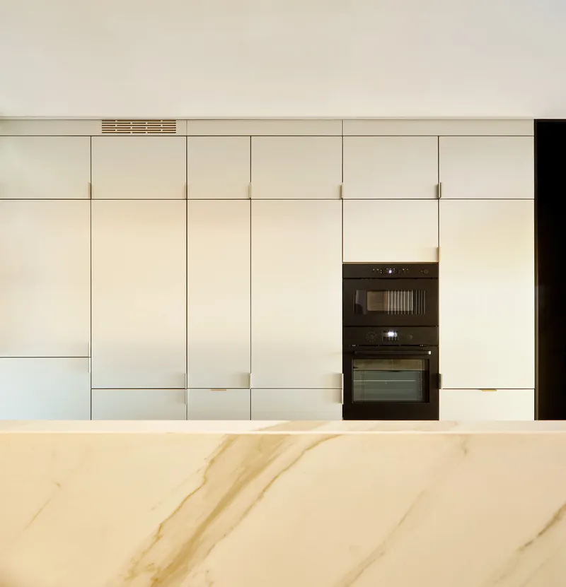 Kitchen island with veined marble countertop in front of flush white cabinetry with integrated appliances
