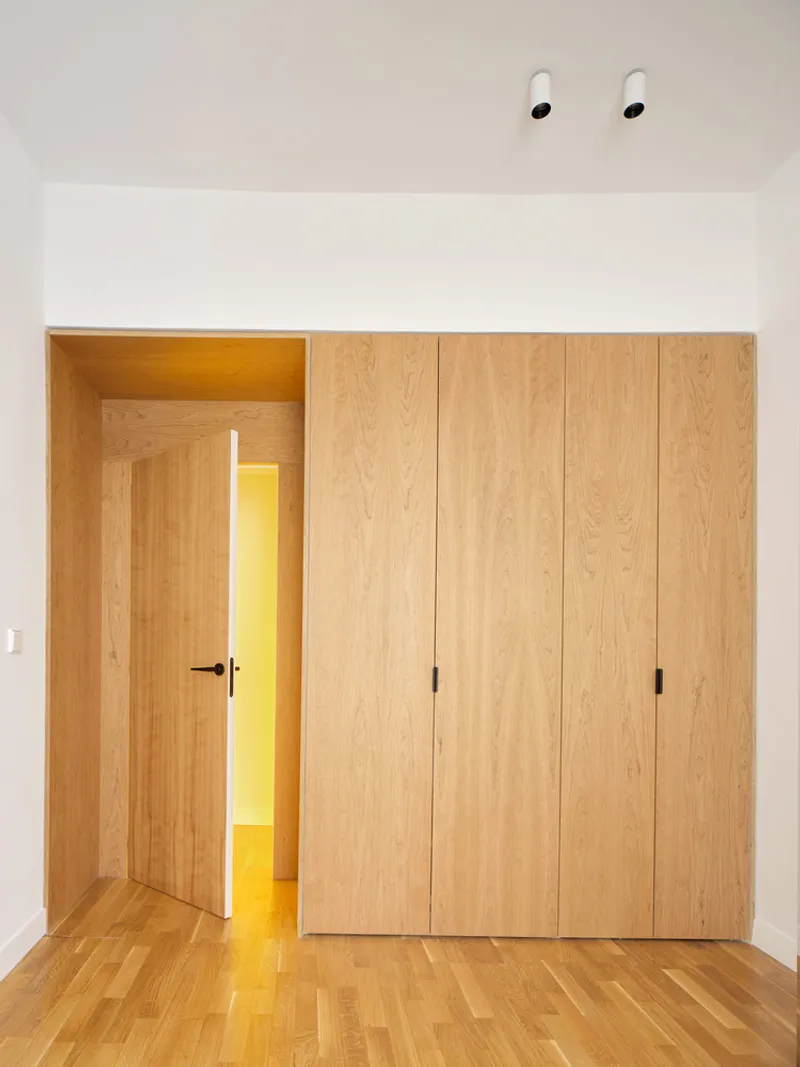 Timber-clad wardrobes and doorway opening to a yellow-lit corridor in a white room