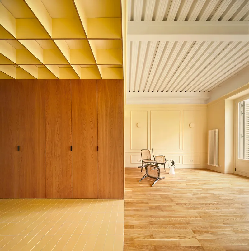 Interior showing yellow geometric coffered ceiling above timber cabinetry and paneled walls with parquet flooring