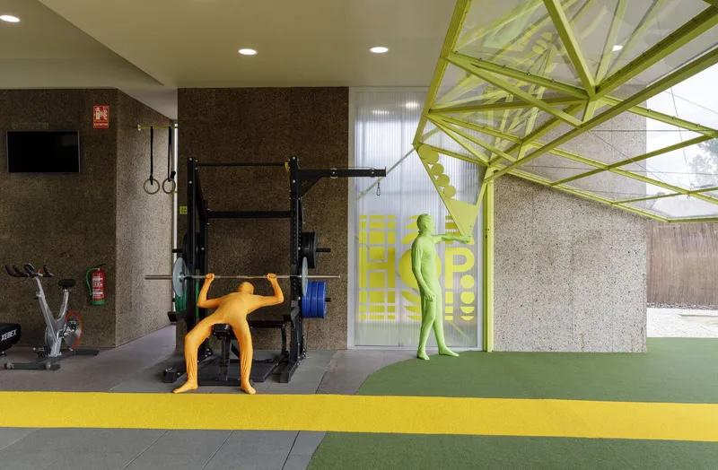 Fitness area with cork walls and lime green steel truss framing glass doors to exterior courtyard