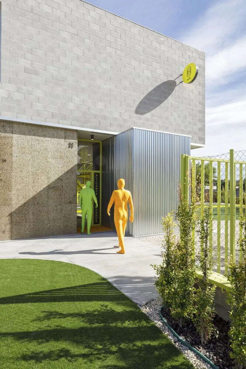 Entry canopy with lime green steel truss and translucent cladding beneath concrete block tower under bright sky