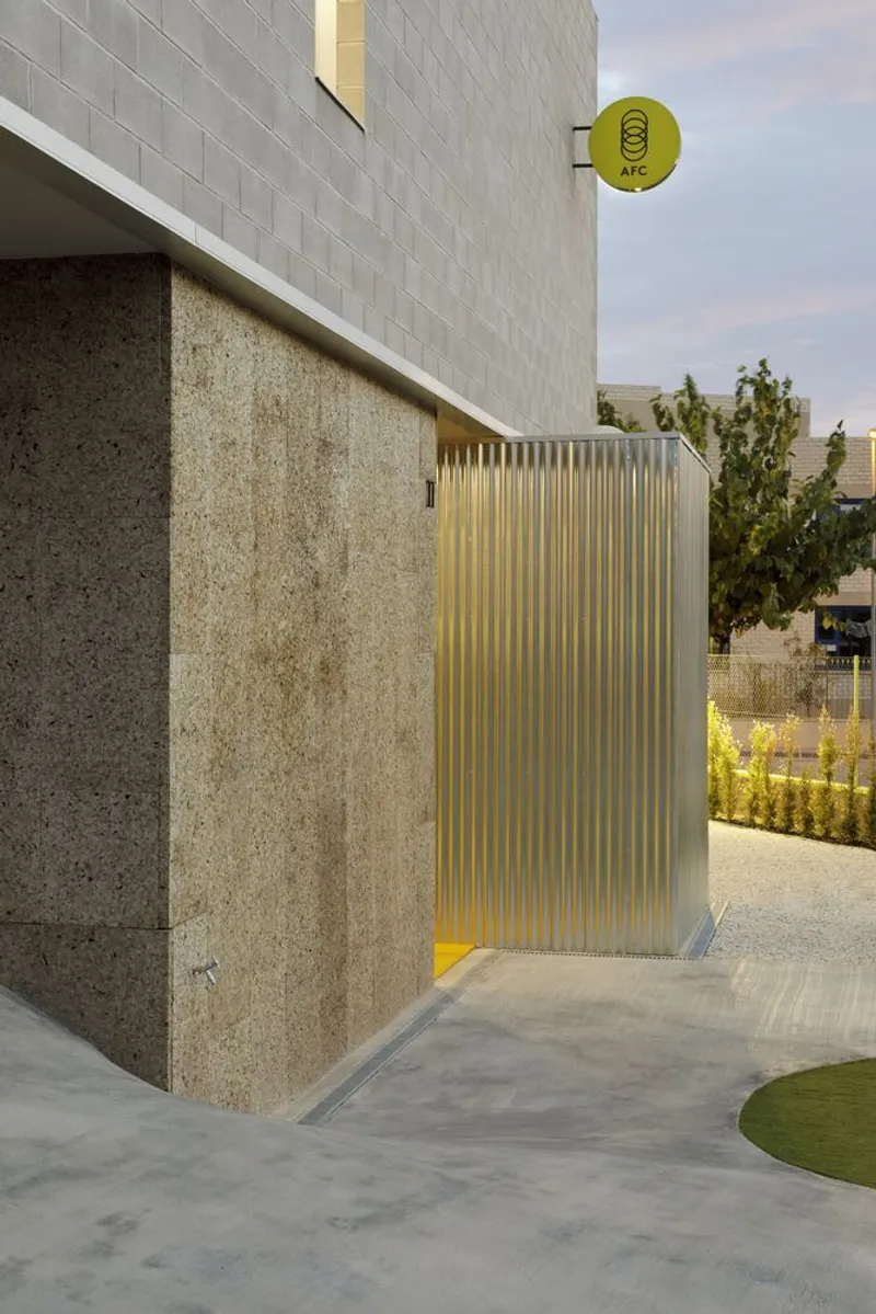 Entry detail showing translucent corrugated panel sliding door with yellow interior glow and round signage above cork-clad wall