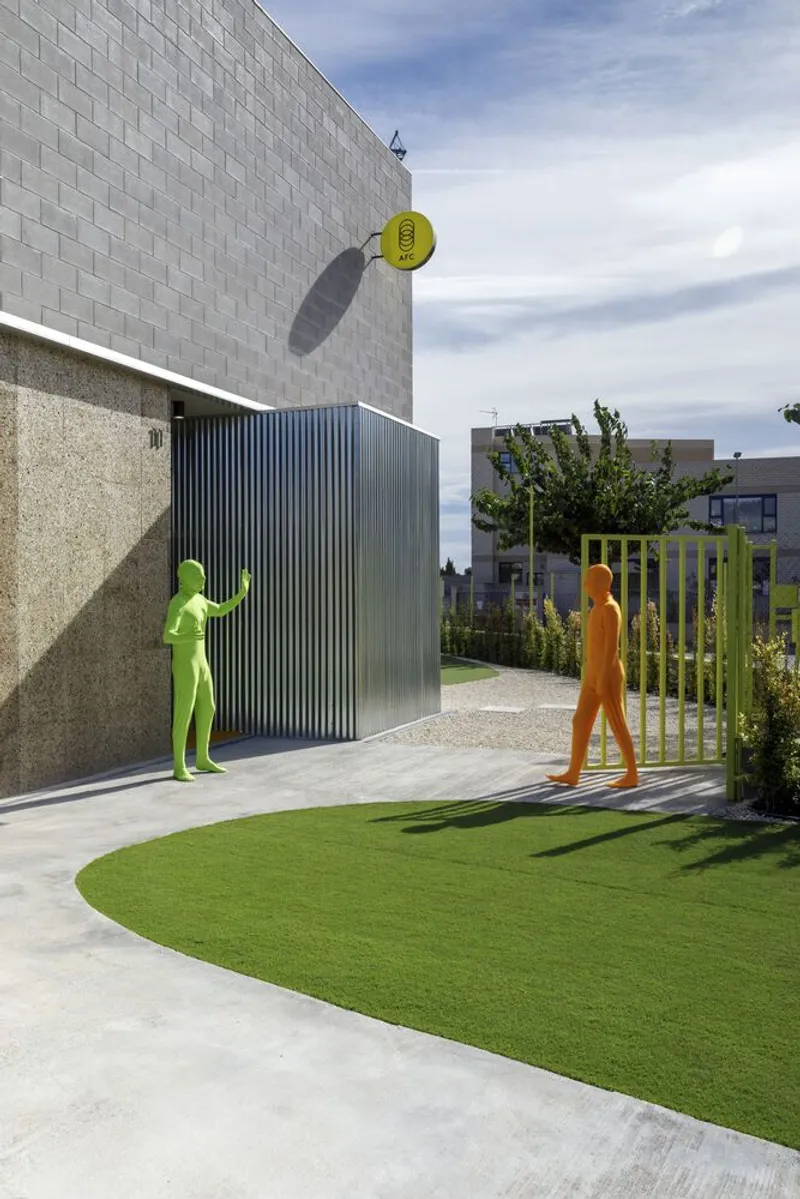 Curved green lawn bordered by concrete pavement with colored silhouette figures beneath cloudy sky