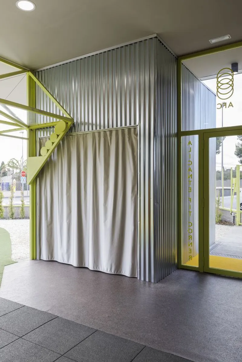 Interior corner showing corrugated metal wall panel with cream fabric curtain and yellow structural beams