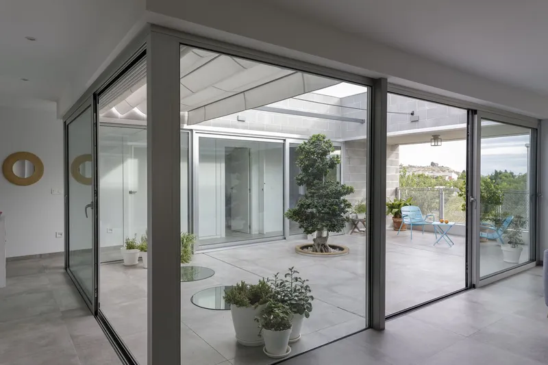 Interior view through sliding glass doors to central courtyard with bonsai tree and potted plants