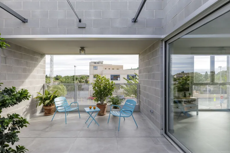 Covered terrace with grey block walls, exposed steel beams, blue folding chairs, and potted plants