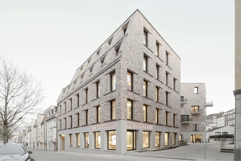 Corner facade with gabled roof and punched windows above a concrete base with illuminated storefronts