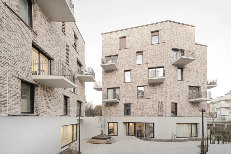 Courtyard view between brick residential blocks with cantilevered balconies and a bare tree in winter