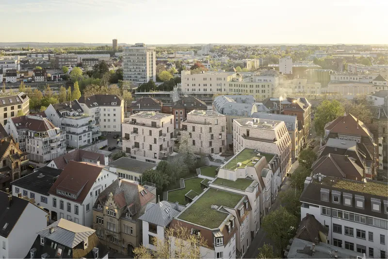 Aerial view showing the pale brick housing complex nestled among low-rise urban buildings at dusk