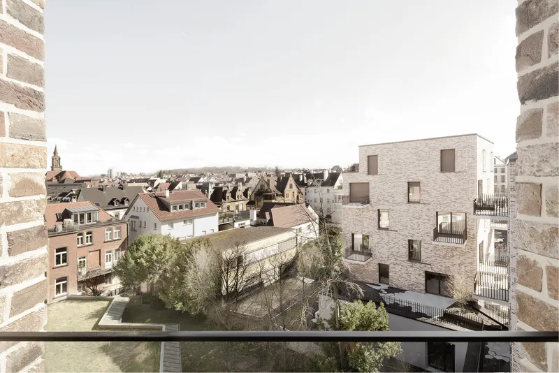 Rooftop terrace framing the brick housing blocks beyond neighboring gardens and red-tiled roofs