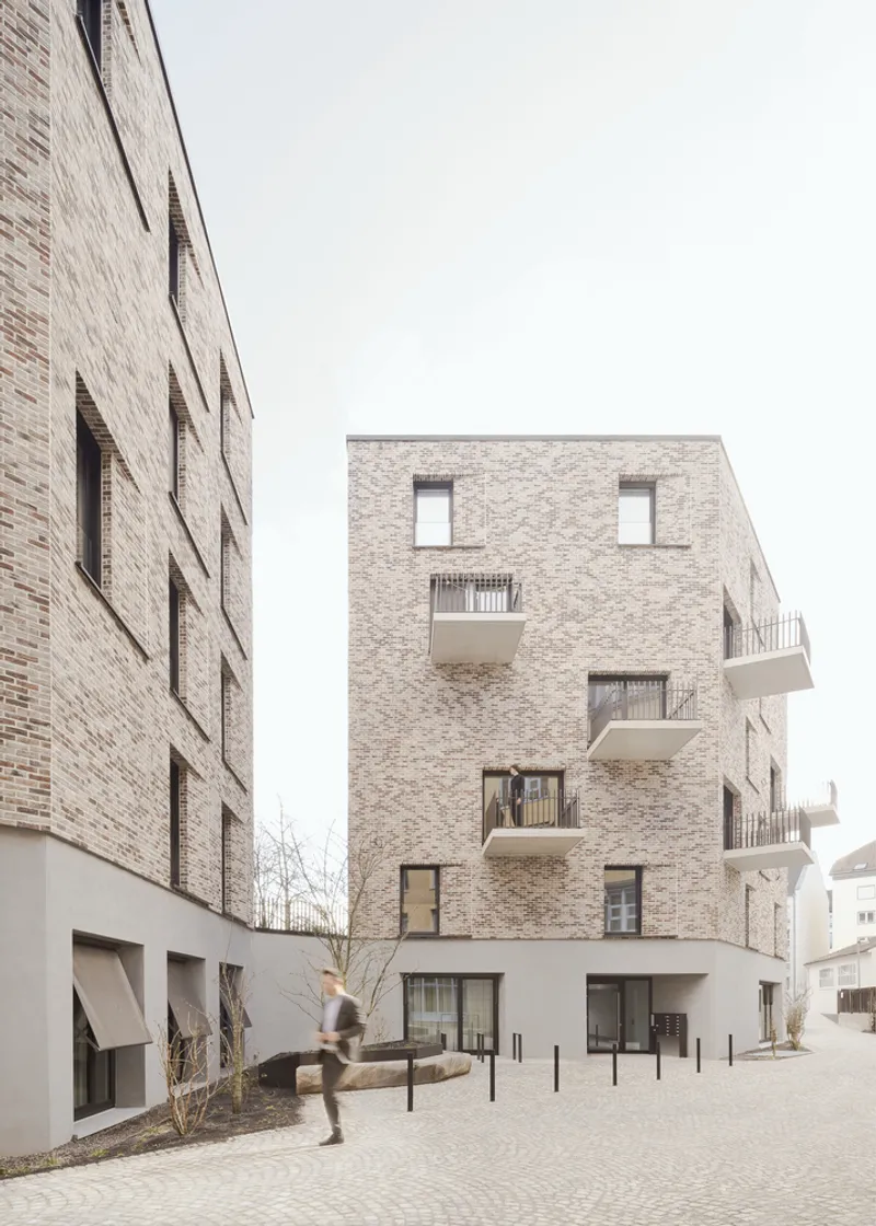 Narrow passage between brick facades showing protruding balconies and a resident walking along the path