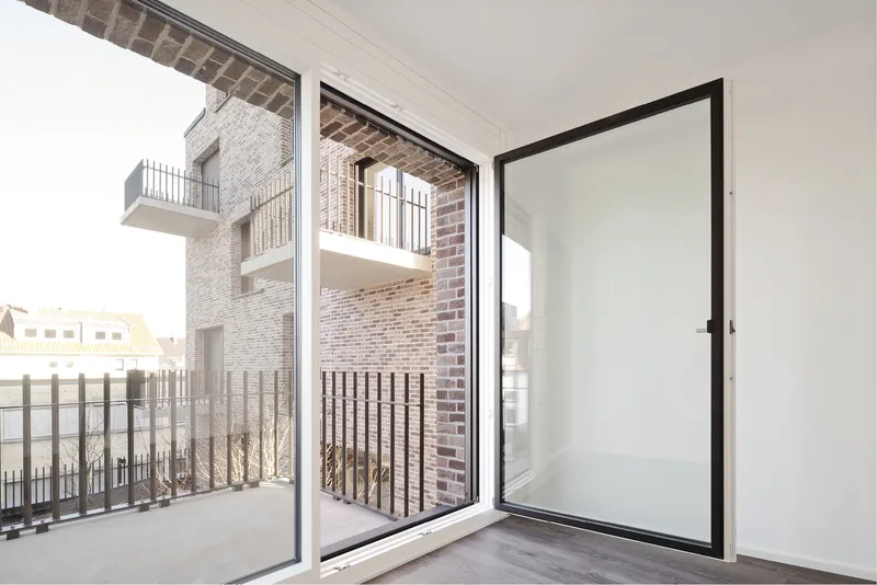 Interior view through open glass doors to a balcony with brick facade and metal railings beyond