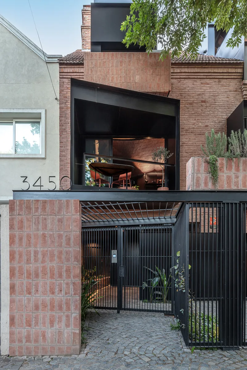 Street view showing black metal gate, terracotta brick wall and elevated terrace with grand piano visible above
