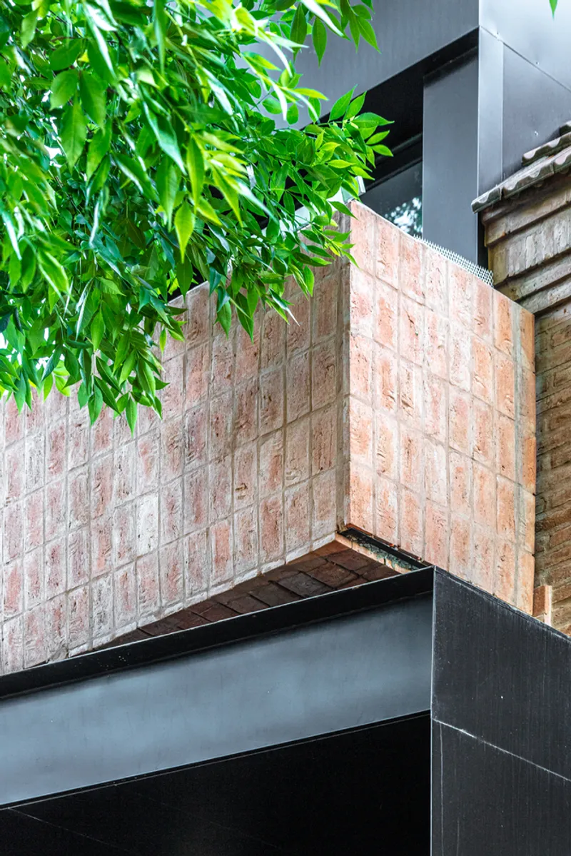 Reclaimed brick planter box with steel frame and overhanging foliage against a gray facade
