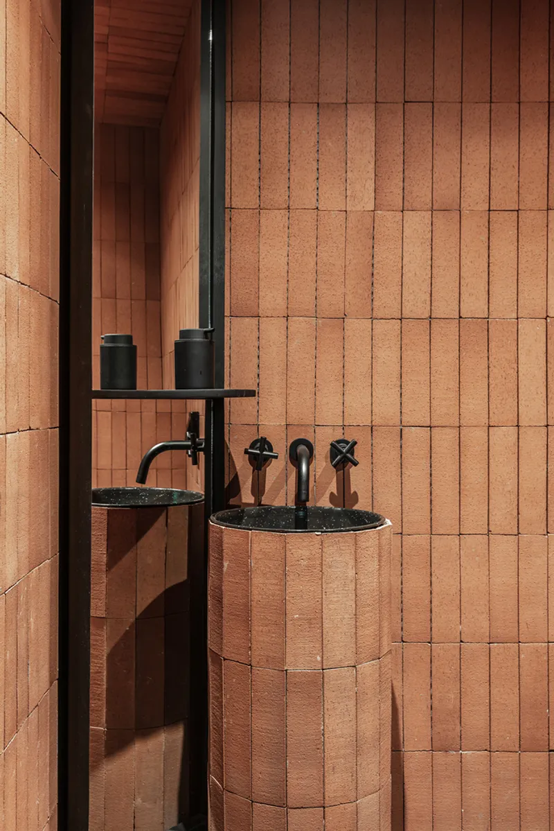 Bathroom detail showing cylindrical basin and wall-mounted fixtures against terracotta tile cladding with black metal trim