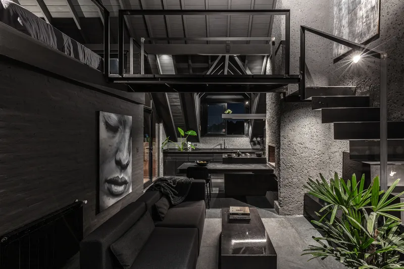 Double height living space with steel mezzanine, textured concrete walls, and illuminated staircase