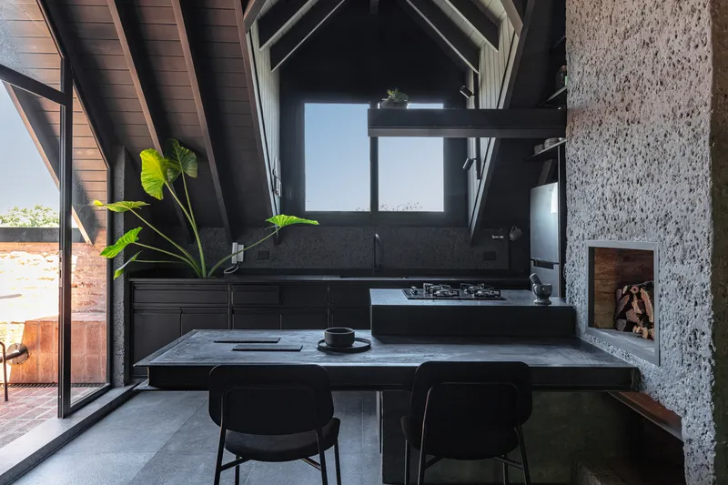 Kitchen with vaulted timber ceiling, black terrazzo island, and doorway opening to brick terrace