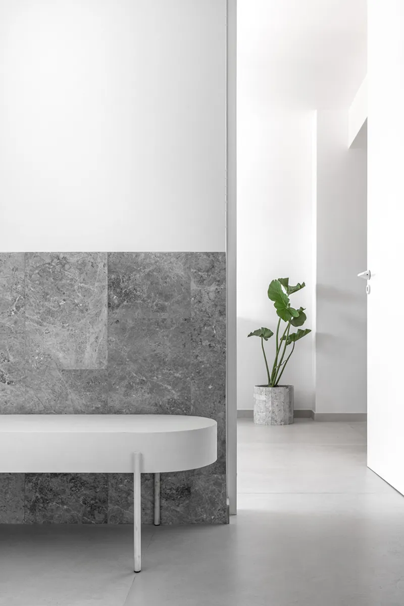 Hallway corner with grey stone wainscoting, white walls, and potted plant beside round table