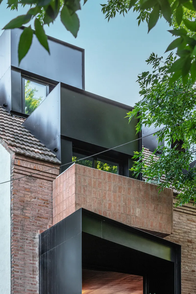 Stacked facade volumes with brick base and dark metal cladding framed by overhanging tree branches