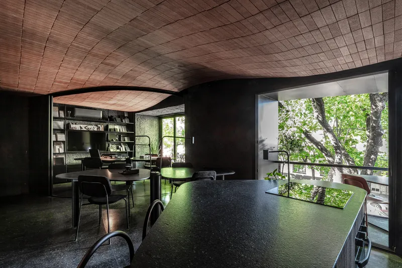 Dining area beneath curved timber ceiling with large window framing outdoor tree canopy