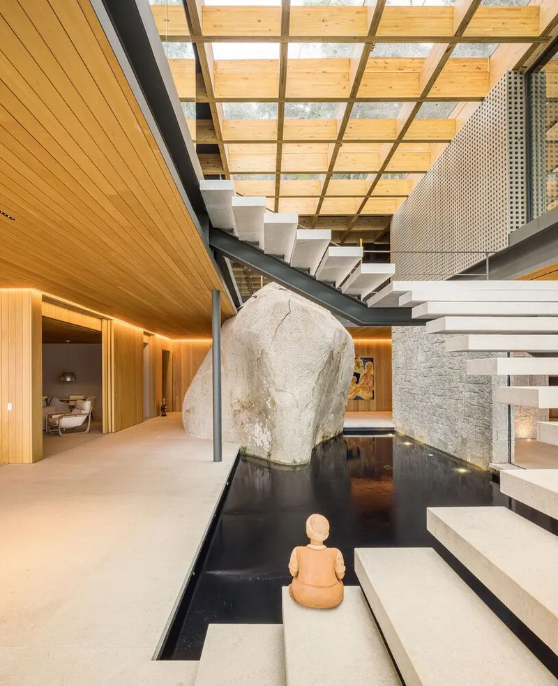 Interior courtyard with floating steel staircase and reflecting pool framed by timber-clad walls and glazed skylight above