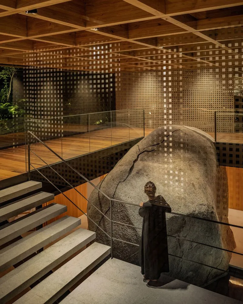 Interior staircase with glass balustrade alongside large granite boulder under perforated brick screens