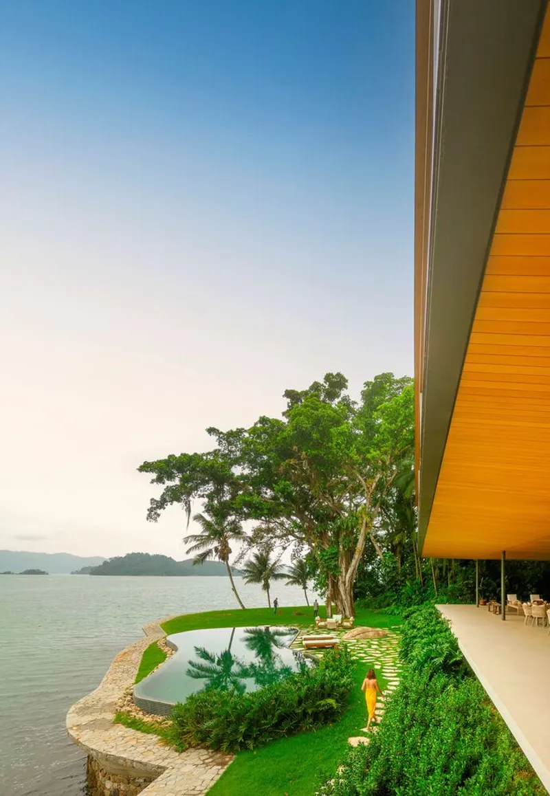 Cantilevered roof edge above a reflecting pool and manicured lawn overlooking a calm bay at dusk