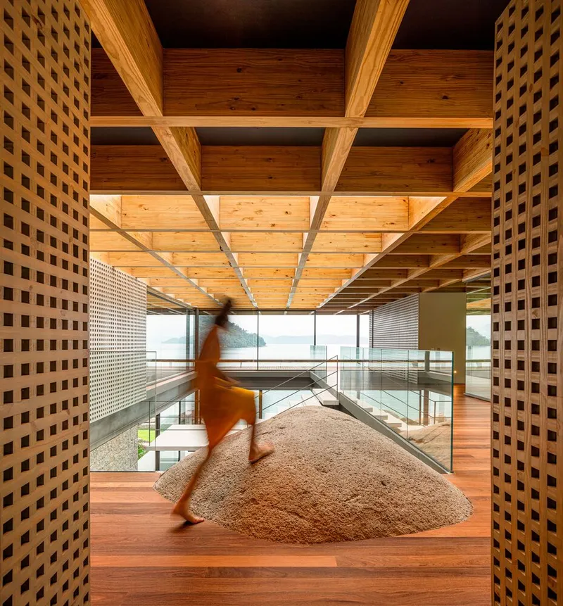 Interior bridge with latticed timber screens and coffered ceiling as a figure walks past a circular rug