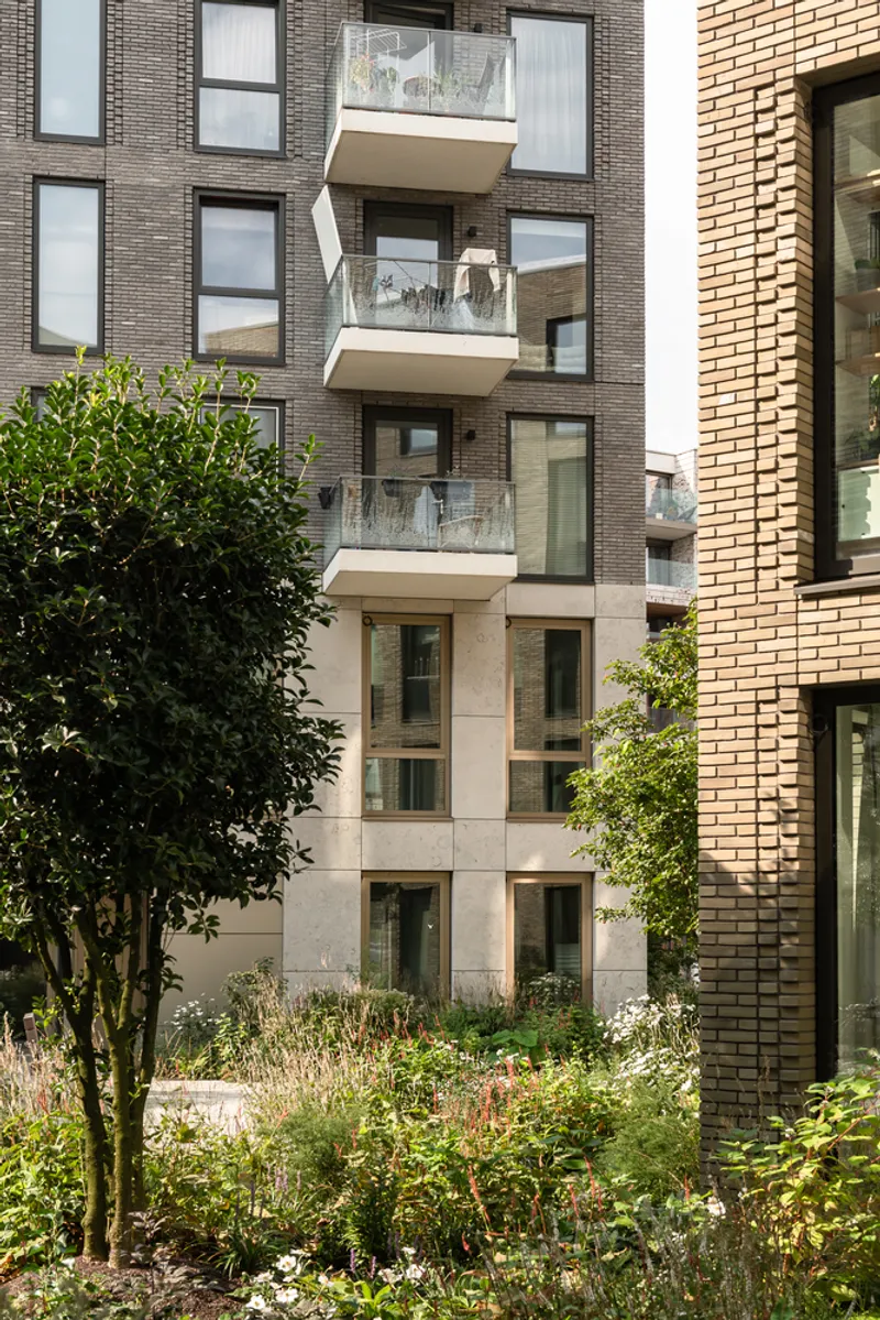 Facade detail showing stacked balconies with glass railings framed by varied brick textures and garden vegetation