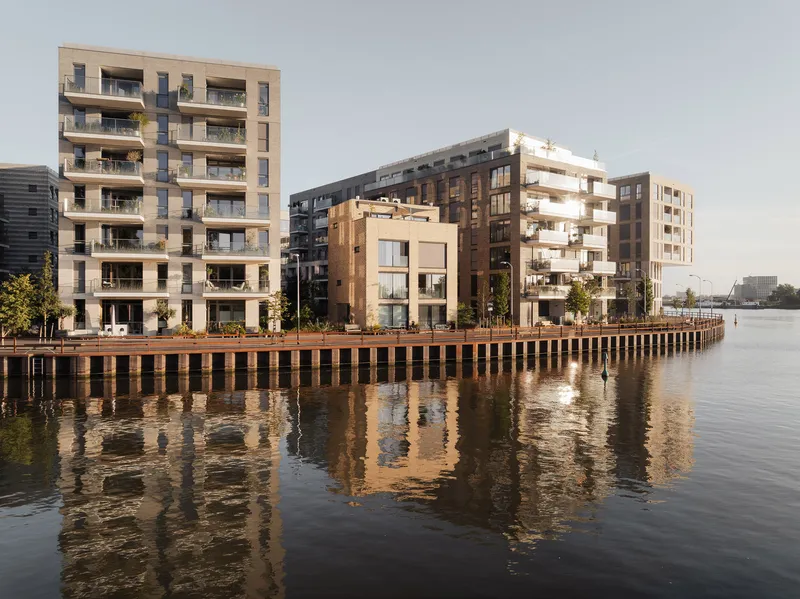 Waterfront facades with balconies and timber pile edge reflected in calm canal water