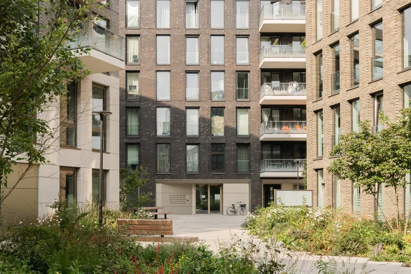 Ground-level entrance with bicycle parking and planted beds between varied brick facades