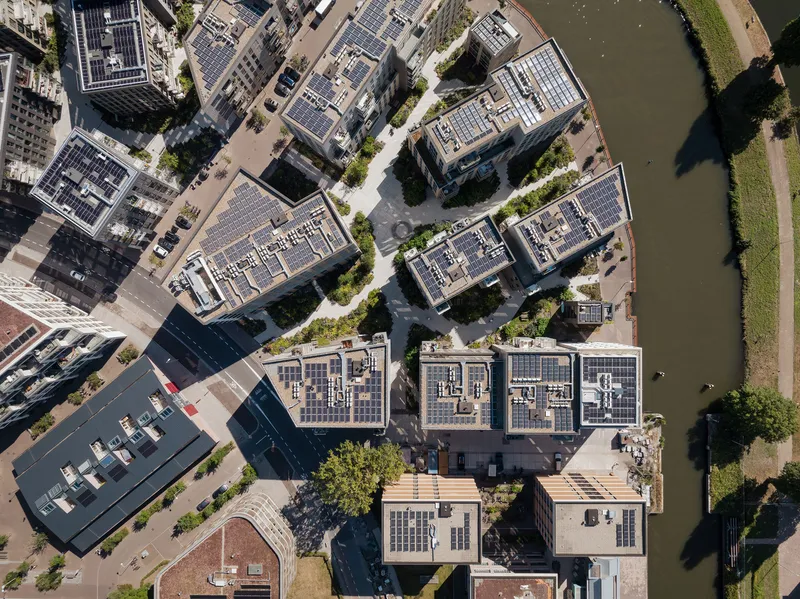 Aerial view of residential blocks with solar panel rooftops arranged around shared courtyards beside a waterway