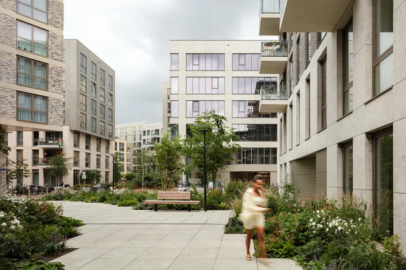 Shared courtyard with planted beds, benches and young trees between brick and cream-clad residential facades