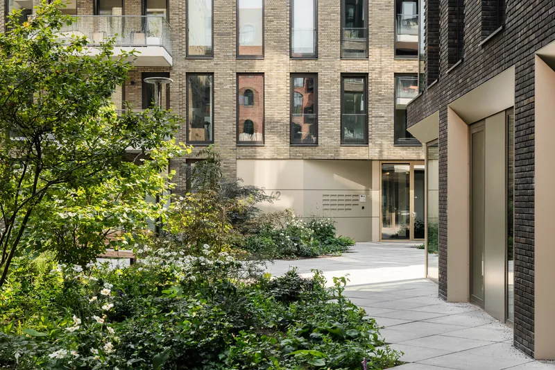 Passage through the residential block framed by dark brick walls and green planting beds