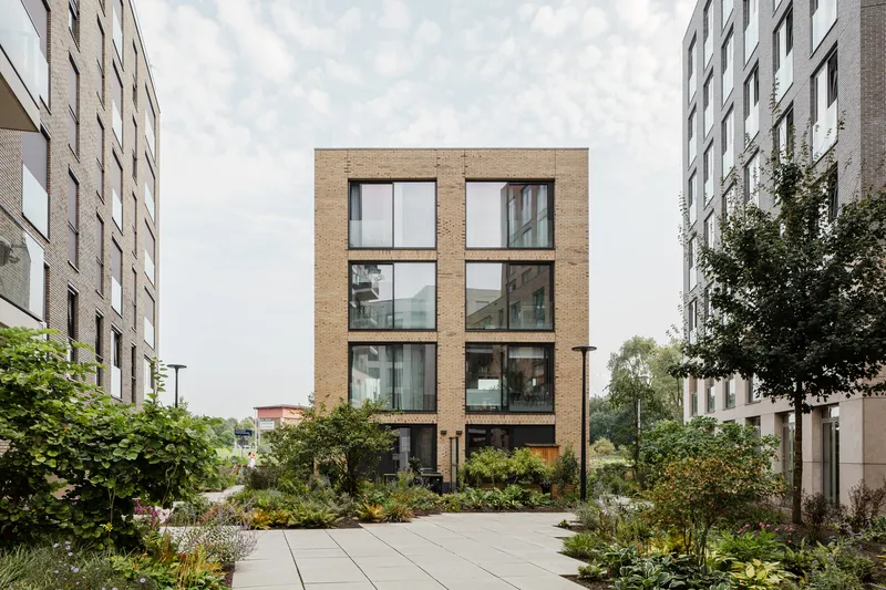 Four-story brick volume with large paired windows framed by landscaped gardens and flanking residential towers
