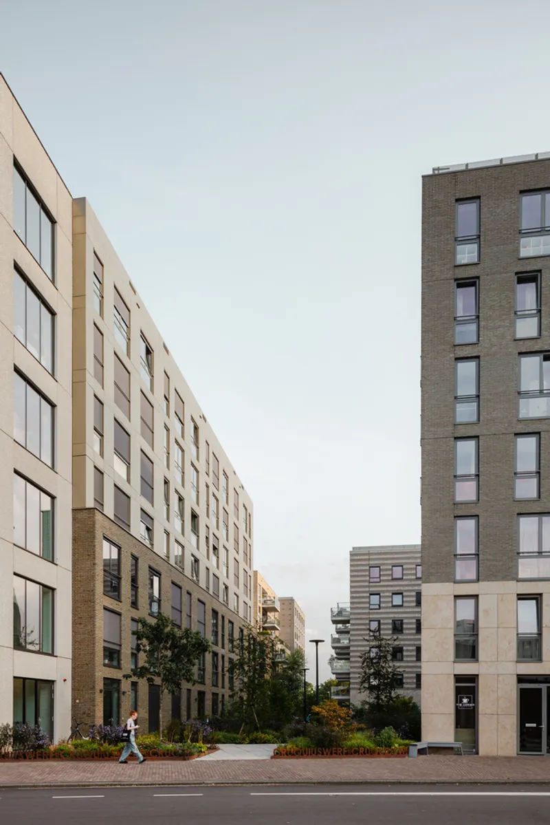 Street facade of the residential block with varied brick tones as a person walks past planted borders