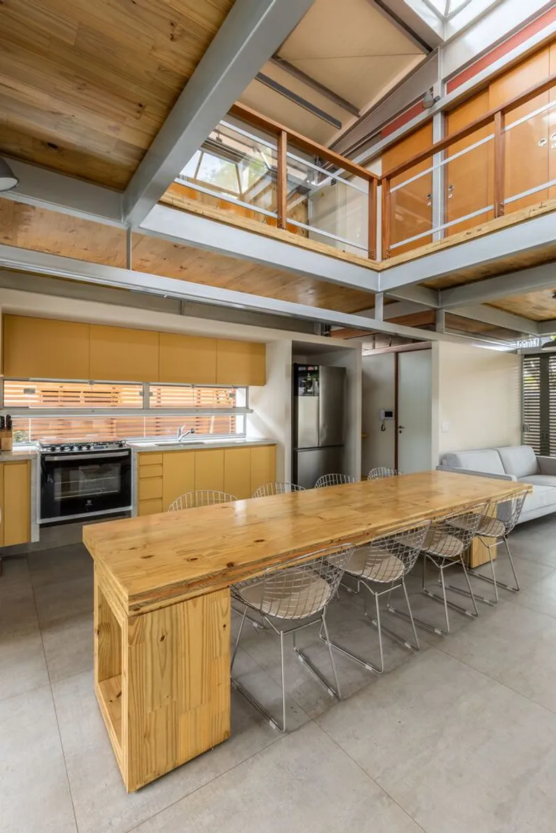 Open kitchen and dining area with timber table beneath mezzanine and exposed steel beams