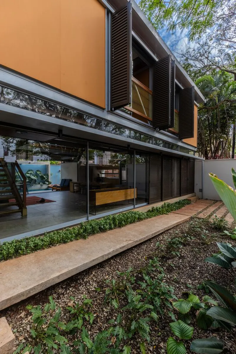 Rear courtyard showing the elevated volume with louvered shutters above planted beds and paving
