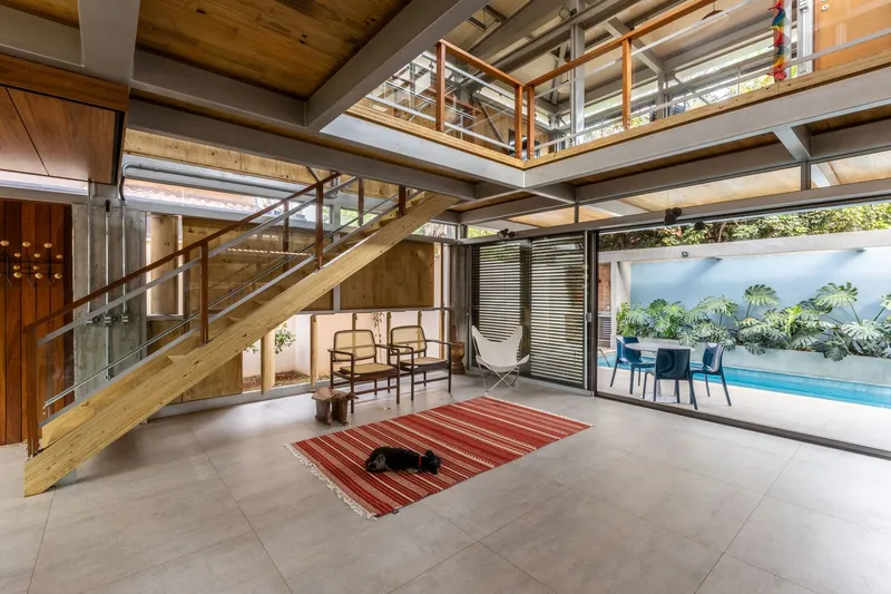 Double-height living space with timber staircase ascending past exposed steel beams and timber ceiling